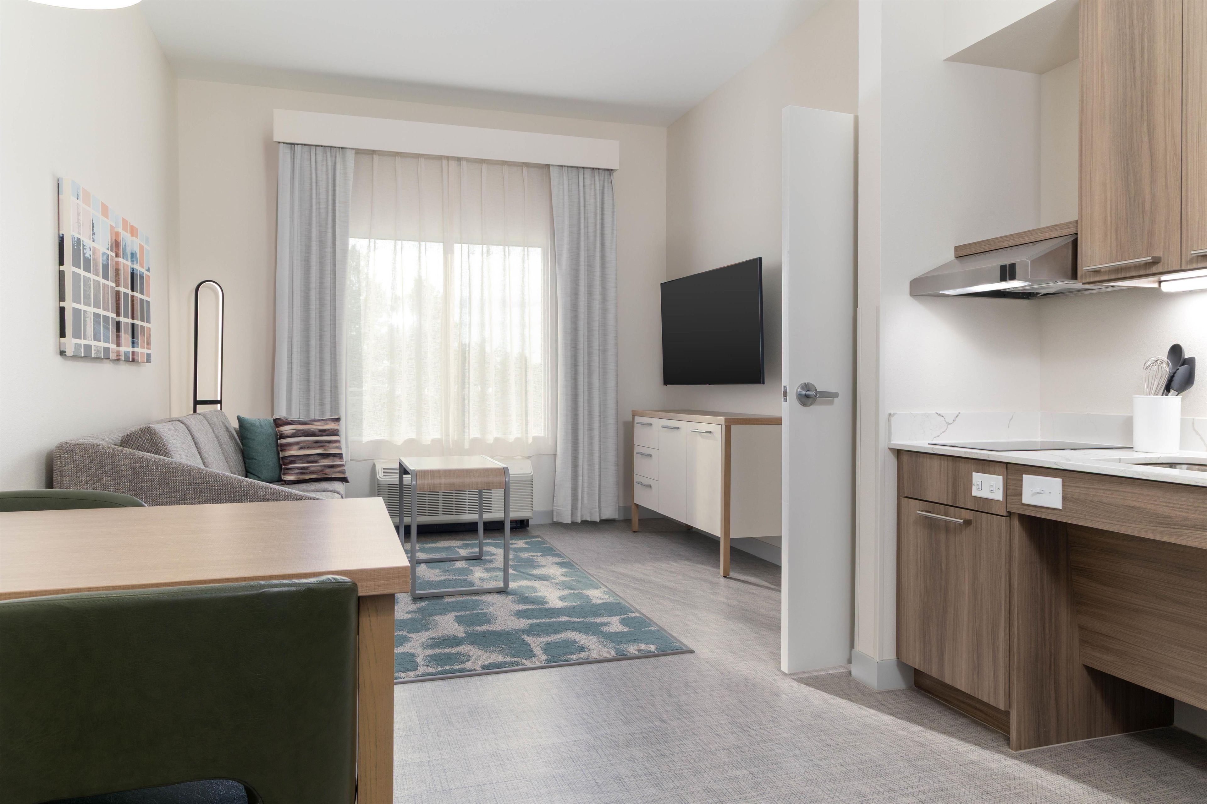 A modern, well-lit room with a dining area, a television, and a kitchen.