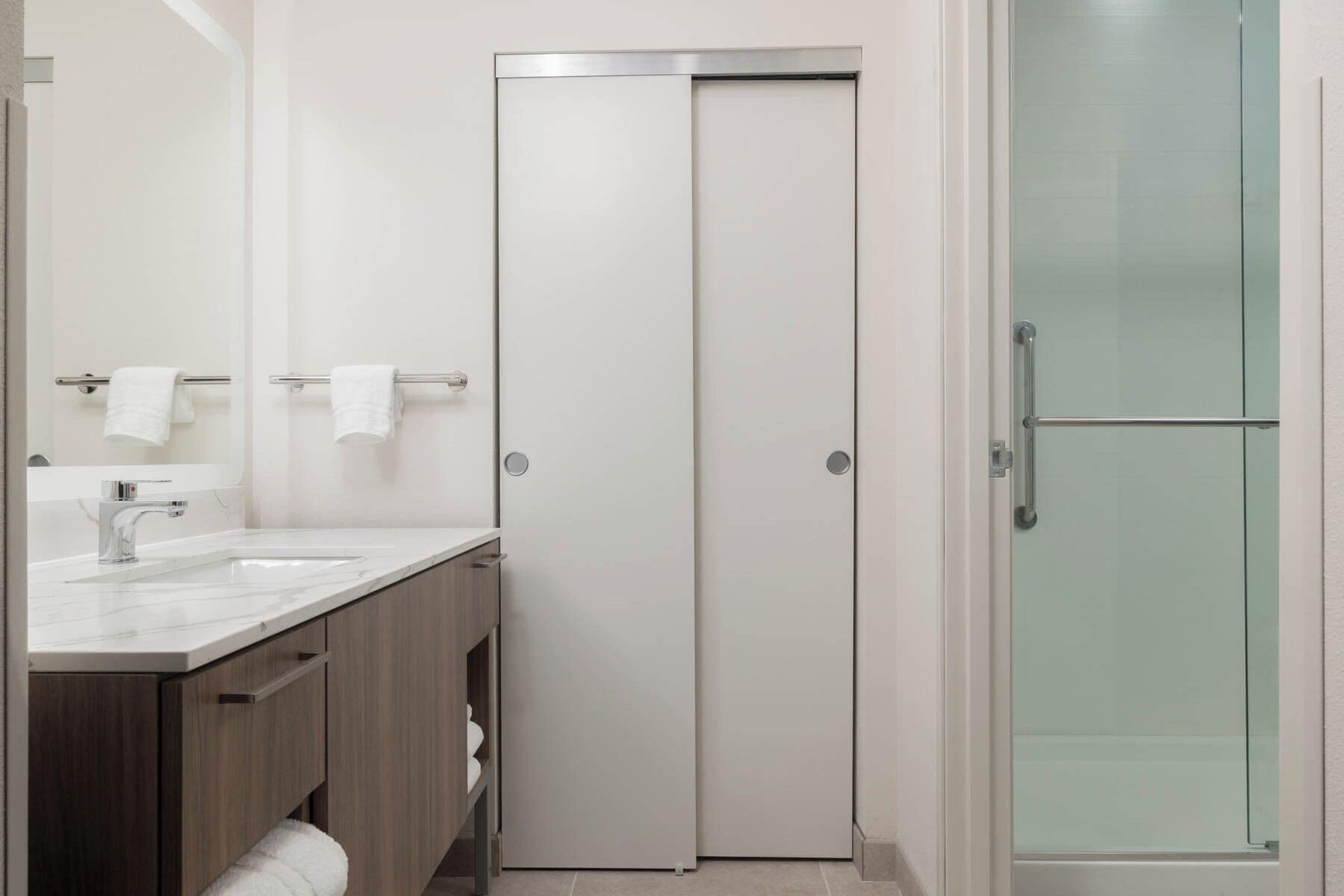Un baño moderno con tocador blanco, cabina de ducha con mampara de vidrio y puerta con manija.
