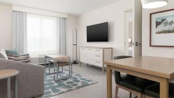 A hotel room with a sofa, a dining table, a TV, and a bed.