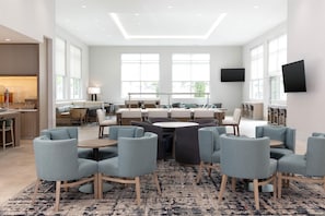 A modern hotel lobby with a central seating area, a bar, and a television mounted on the wall.