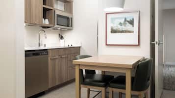 Cocina compacta con microondas, pileta y alacenas. Hay un cuadro en la pared y una mesa con sillas.