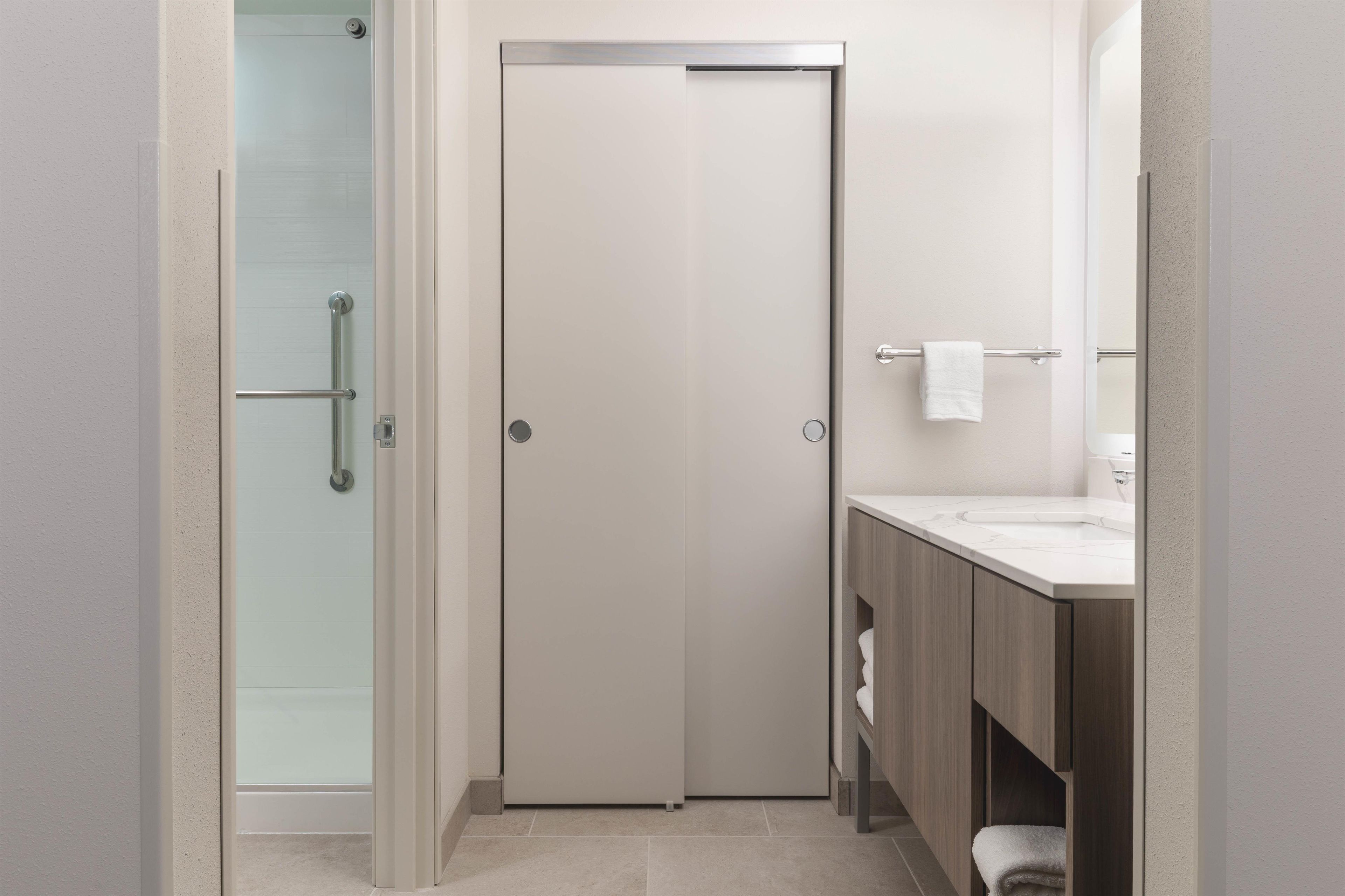 A modern bathroom with a glass shower enclosure, a white door, and a vanity with a towel rack.