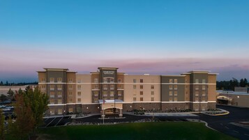 Edificio de un hotel de varios pisos con un llamativo letrero de 'Homewood Suites by Hilton', un estacionamiento y un área ajardinada al frente.