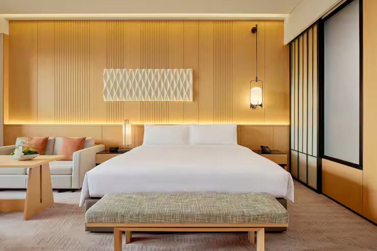 Ein modernes Hotelzimmer mit einem großen Bett, einem Nachttisch, einer Lampe und Blick ins Freie.