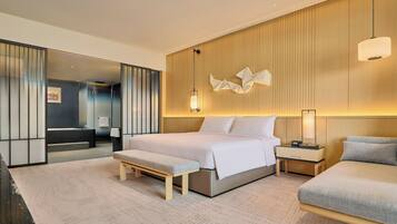 A modern hotel room with a large bed, a smaller bed, a bench, a nightstand, and a mirror.