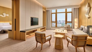 Ein modernes Hotelzimmer mit großem Fenster, Flachbildfernseher, einer Couch, einem Esstisch und zwei Stühlen.