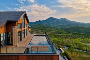 A modern building with a rooftop pool, large windows, and a view of a mountainous landscape. - Secan Hotel Qingdao, Curio Collection By Hilton (Qingdao)