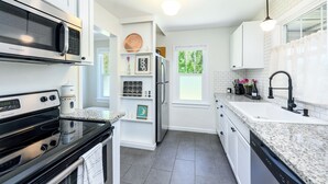 A modern kitchen with white cabinetry, a stainless steel refrigerator, a built-in microwave, and a granite countertop.