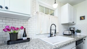 A kitchen with white cabinets, a granite countertop, a sink, a toaster, and a potted plant.