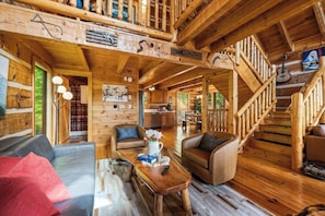 A wooden cabin interior with a dining area, seating, and a staircase.