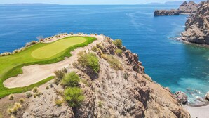Un campo de golf costero con vistas despejadas al mar y montañas a lo lejos.