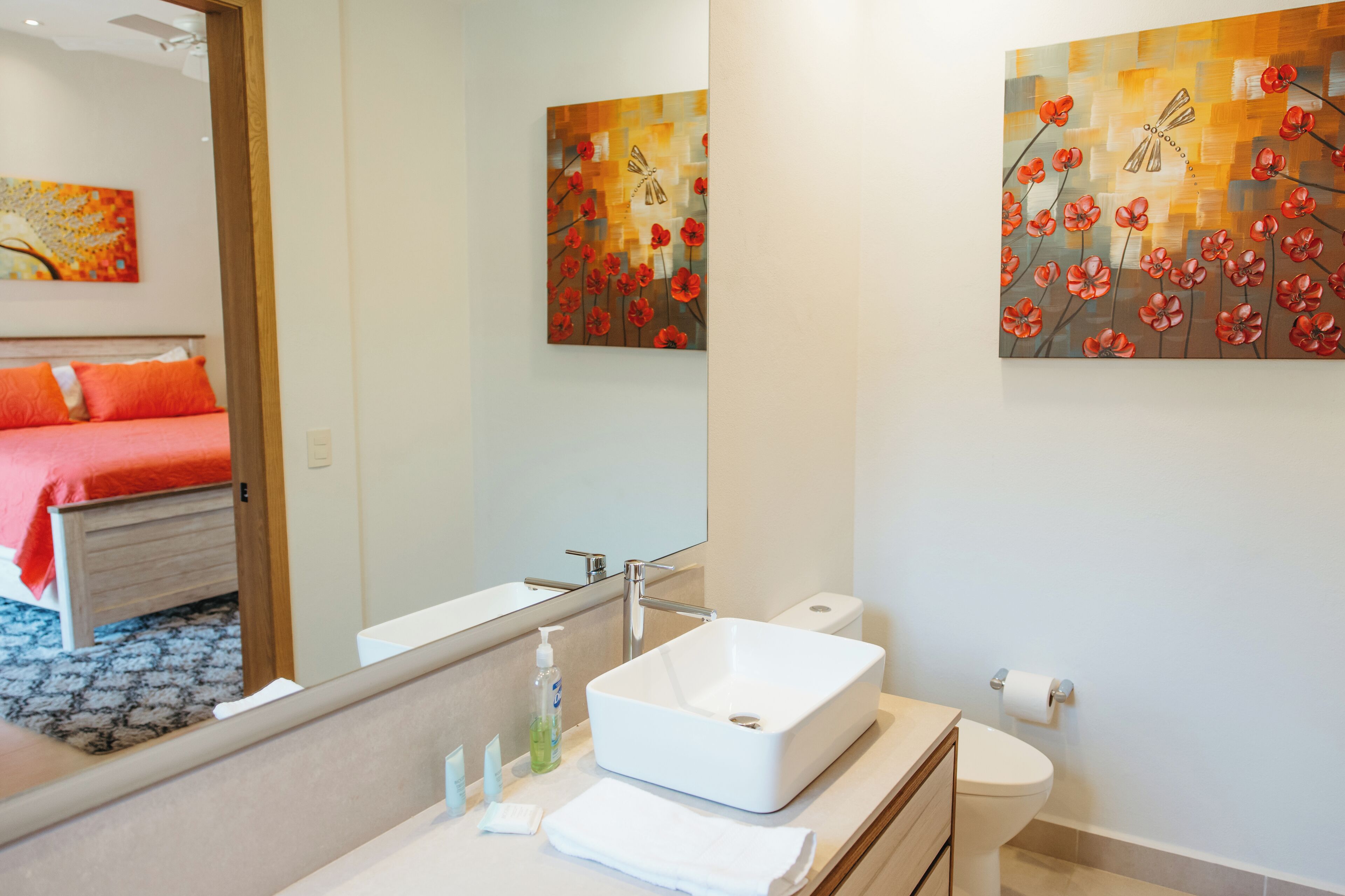 Une salle de bain moderne avec un lavabo blanc, un miroir et des toilettes. Un tableau représentant des fleurs rouges est accroché au mur.