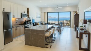 Una cocina moderna con una isla central, un comedor con vistas al océano y una sala de estar con un amplio ventanal que da a la playa.