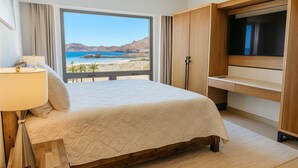 Un dormitorio con cama, escritorio, televisor y vista a la playa.