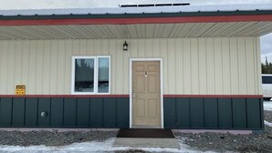 A building with a beige exterior, a red and green trim, a single door, and a window.