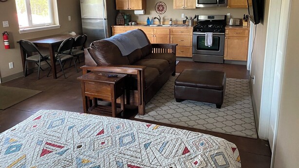 A compact kitchen with wooden cabinets, a refrigerator, microwave, stove, and a dining area with a table and chairs.