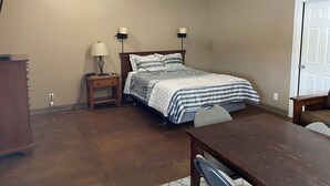 A bedroom with a bed, bedside lamps, a wooden nightstand, a dresser, and a wooden table. - Tundra Apt #2-Modern Comfort in the Last Frontier (For families or casual travelers) (Tok)