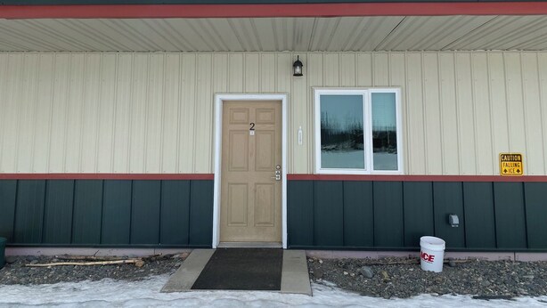 A building with a beige exterior, a red trim, a wooden door, a window, and a caution sign for falling ice. - Tundra Apt #2-Modern Comfort in the Last Frontier (For families or casual travelers) (Tok)