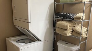 A compact laundry area with a washer and dryer, a toilet, and a metal shelf with towels. - Tundra Apt #2-Modern Comfort in the Last Frontier (For families or casual travelers) (Tok)