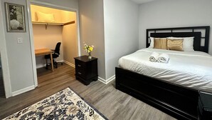 Een slaapkamer met een bed, een bureau, een stoel, een nachtkastje en een vloerkleed.