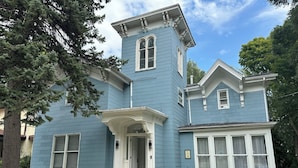 Een blauw huis met twee verdiepingen, een centrale ingang, een klein terras en een schoorsteen.