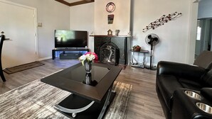 Een woonkamer met een flatscreen televisie, een open haard, een kroonluchter en een leren bank.