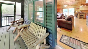 Une cabane en bois dotée d’un porche agrémenté de fauteuils Adirondack, d’un canapé en cuir marron et d’un coin cuisine avec des armoires en bois et une table à manger.