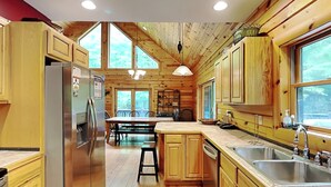 Une cuisine rustique, située dans une cabane en bois, équipée d’un réfrigérateur, d’un évier et de meubles de rangement en bois.