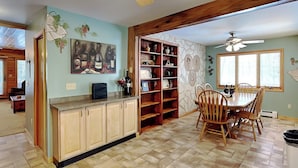 Een keuken met houten kasten, een eettafel met stoelen, een boekenkast en een plafondventilator.