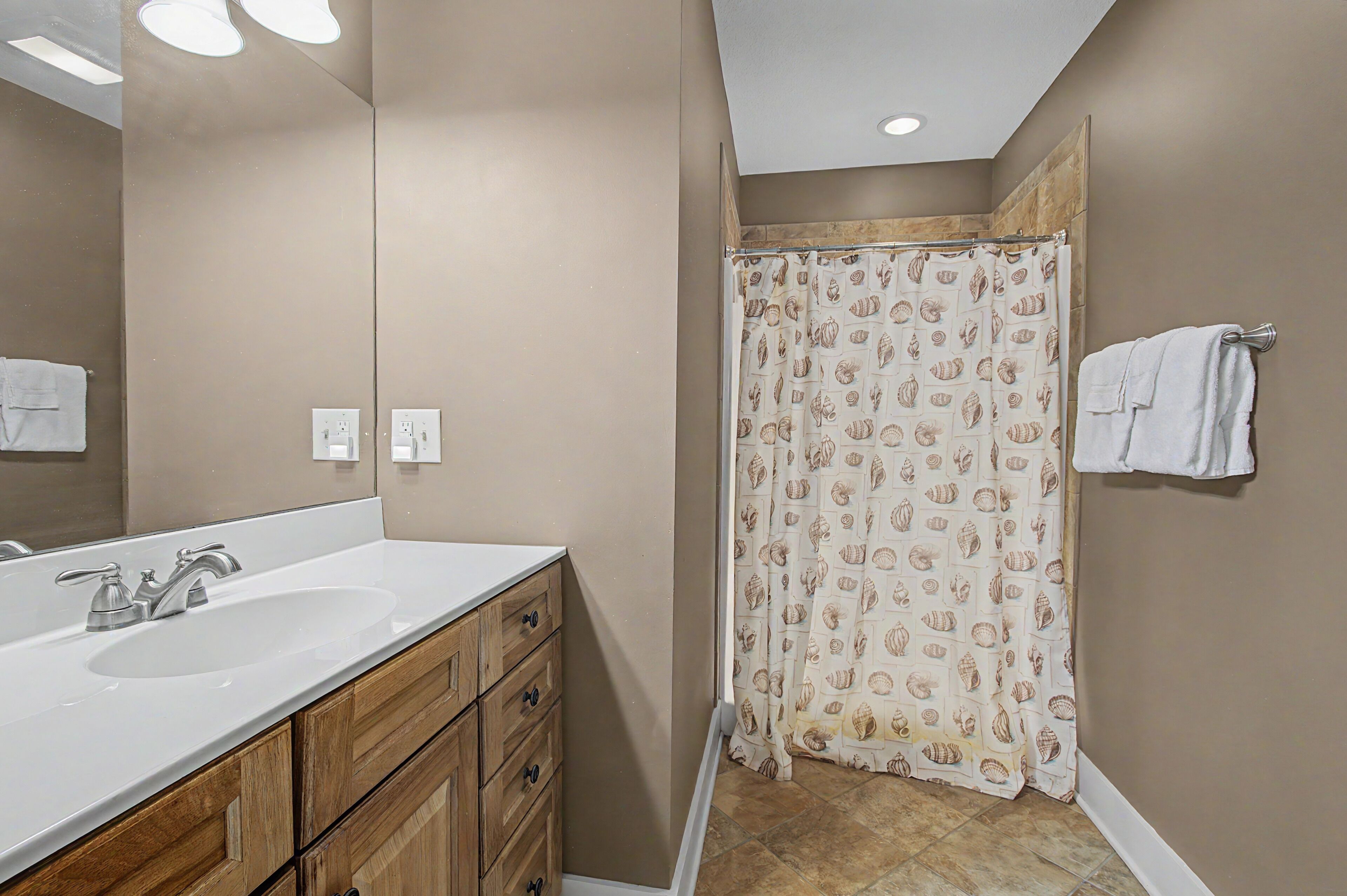 A bathroom with a white sink, wooden cabinets, a shower curtain with a shell pattern, and a towel rack with a towel.