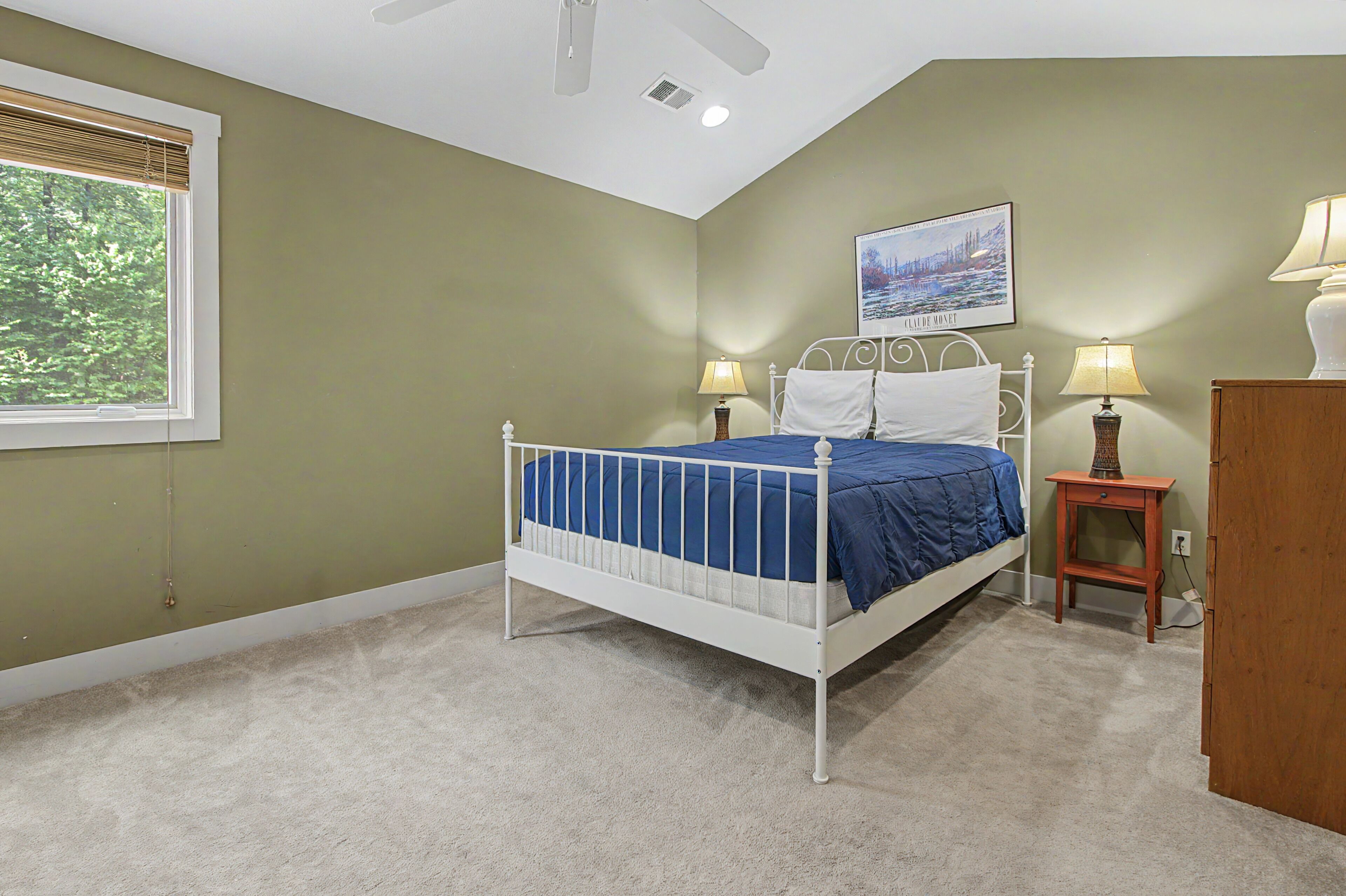 A bedroom with a single bed, two bedside lamps, a nightstand, a window with blinds, and a ceiling fan.