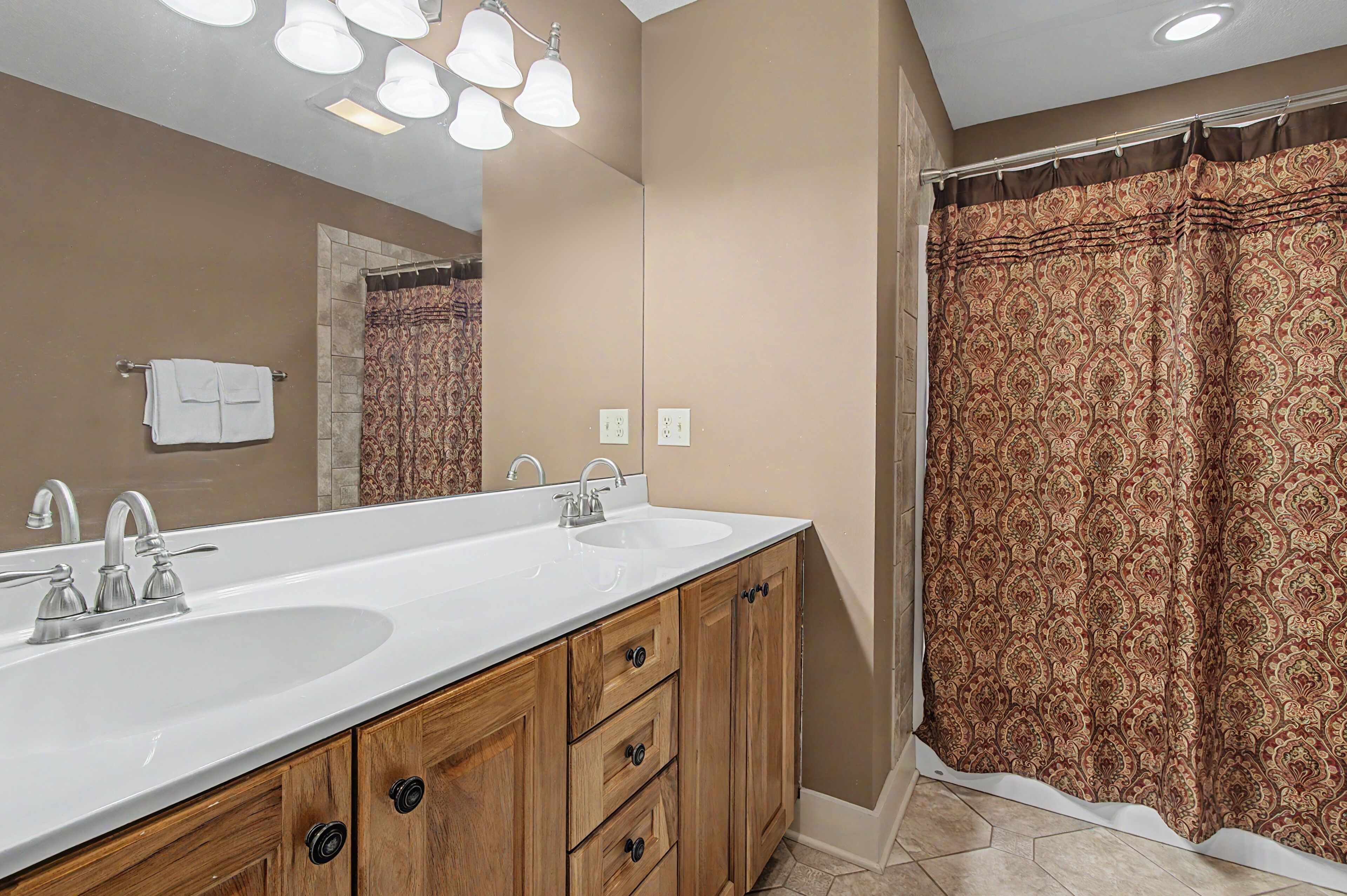 A bathroom with a double sink, wooden cabinets, a mirror, and a shower curtain.
