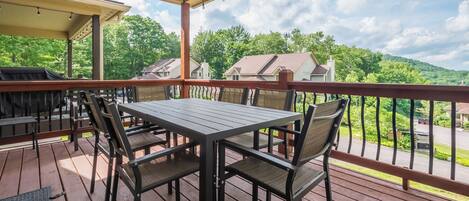 A covered outdoor deck with a table and chairs, overlooking a residential area and hills.