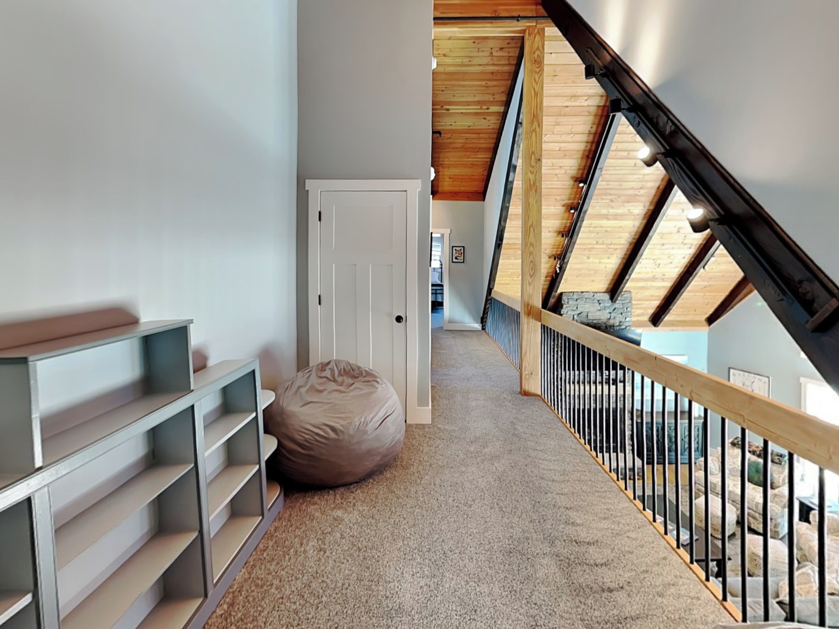 A hallway with a high ceiling, wooden beams, a white door, and a bean bag chair.