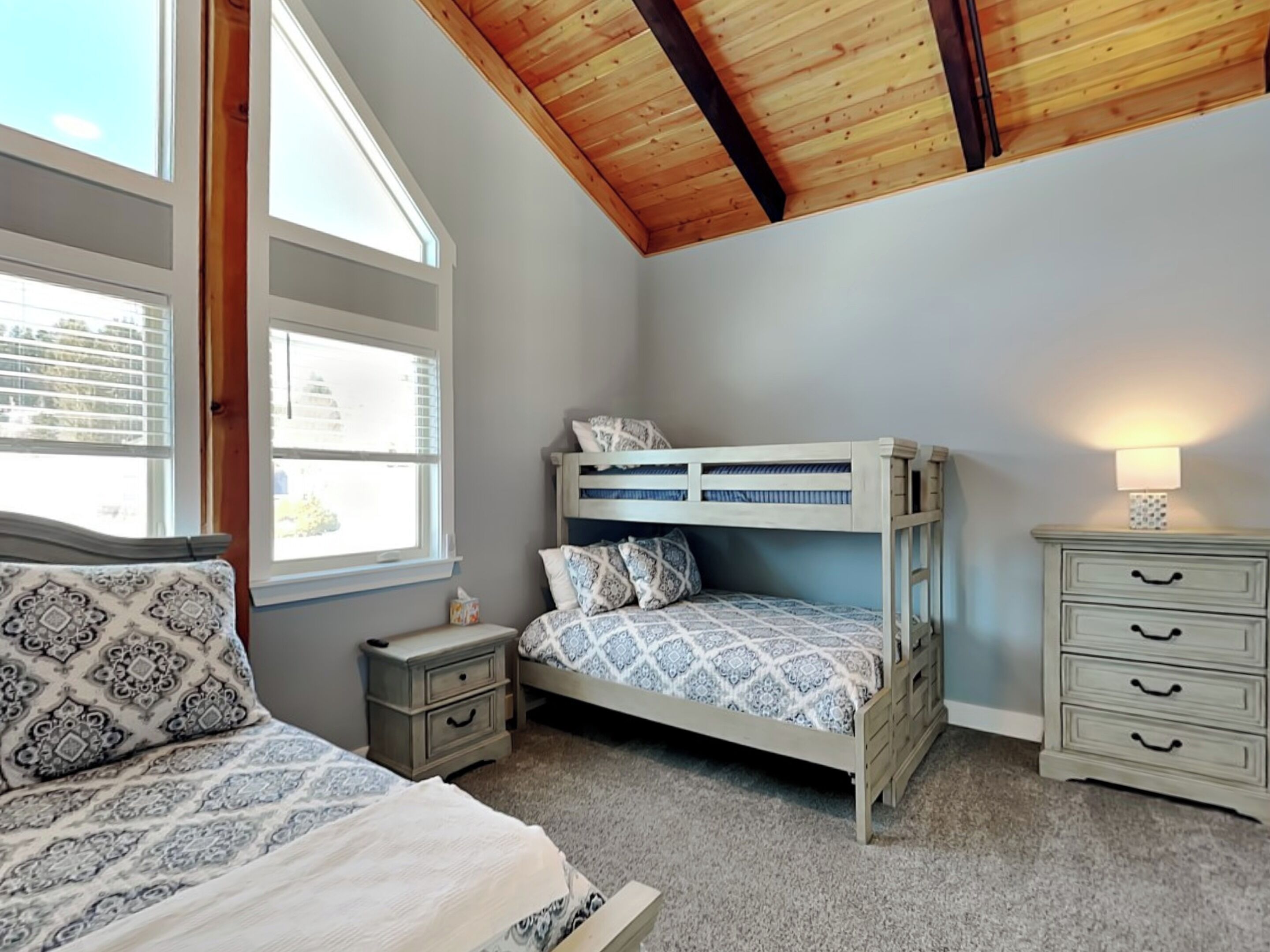 A bedroom with a bunk bed, a bedside table, a nightstand, and a dresser.