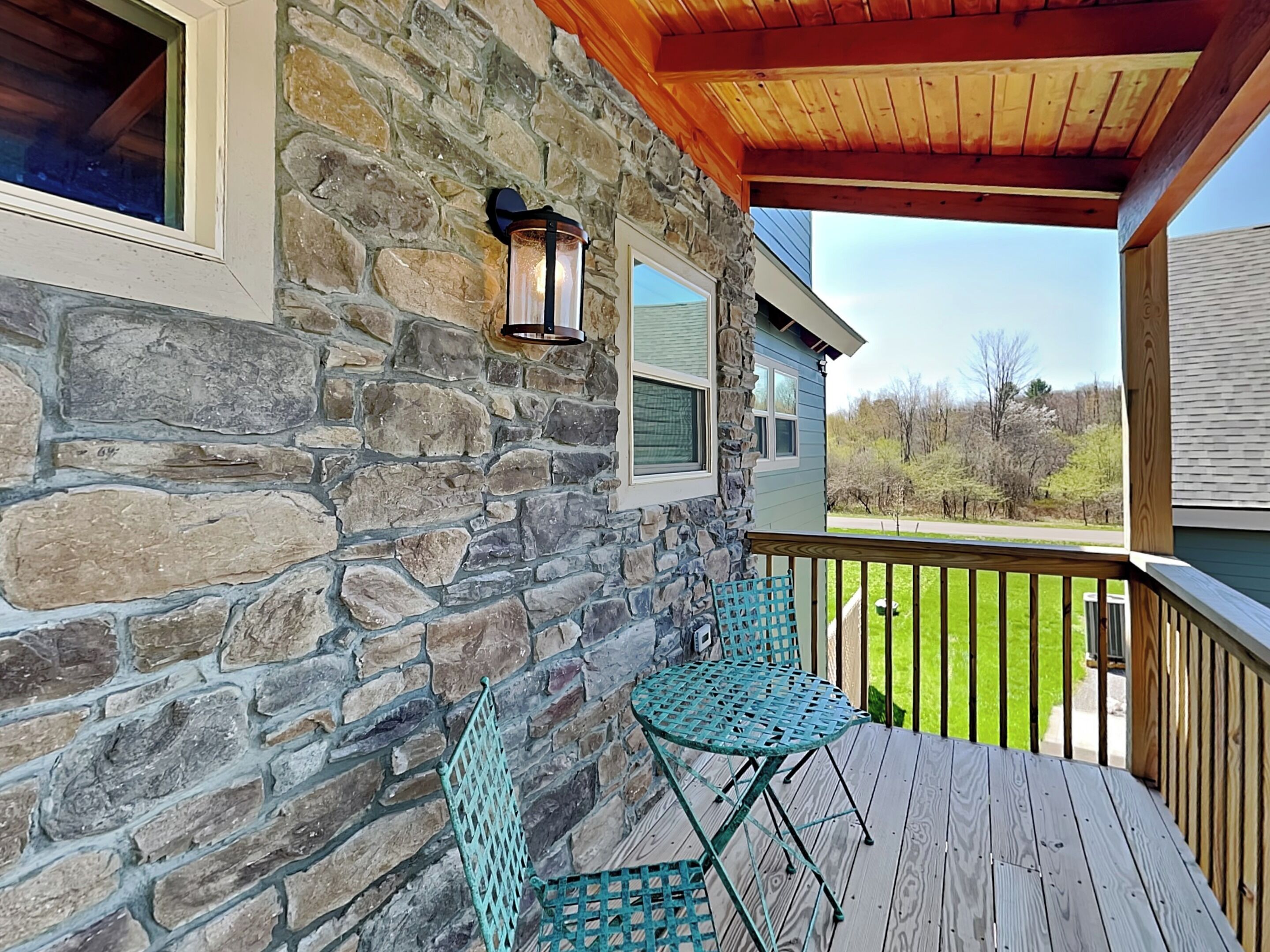 A stone exterior wall with a wooden deck and a metal table and chair.