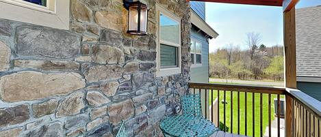 A stone exterior wall with a wooden deck and a metal table and chair.
