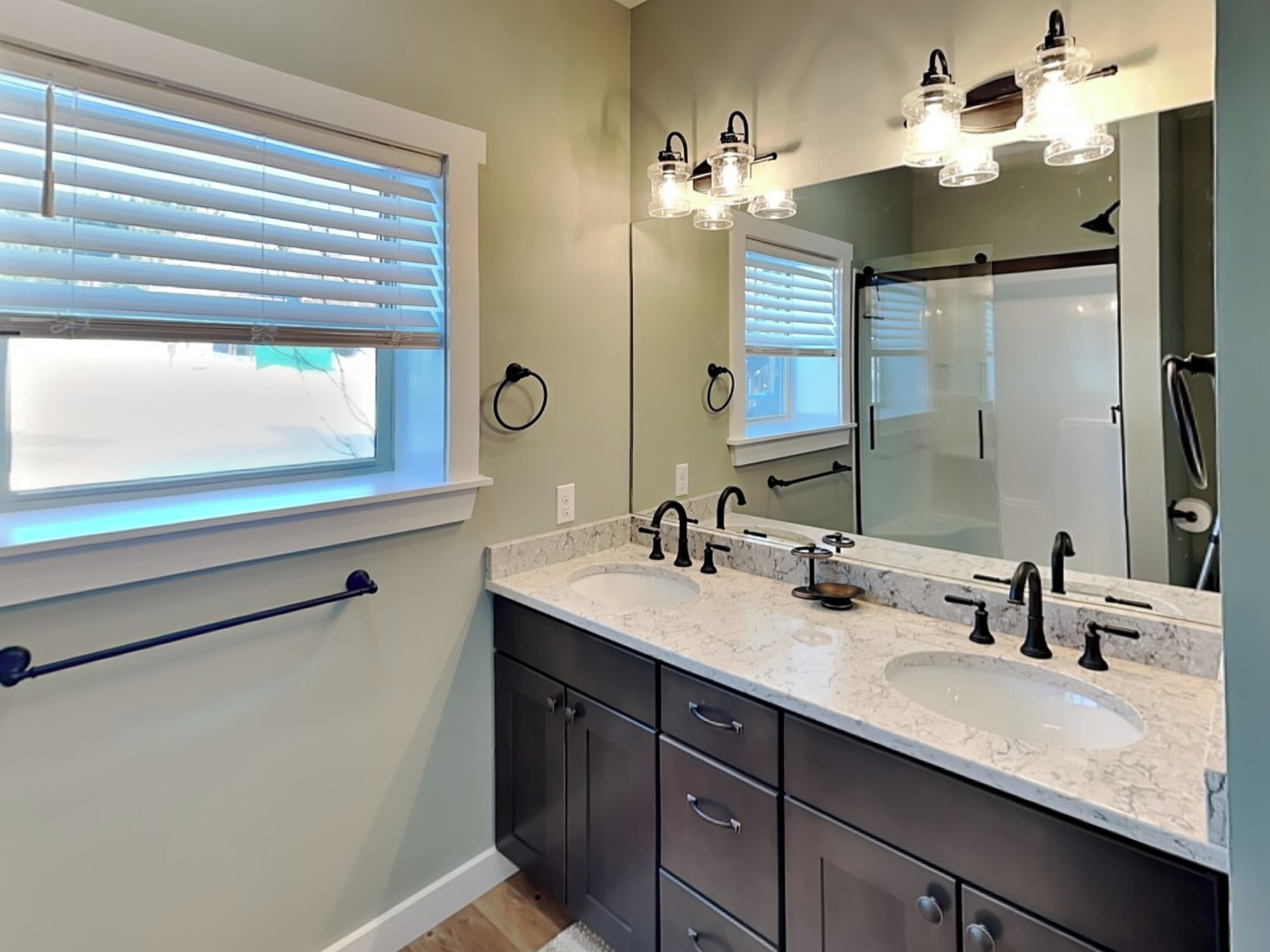 A modern bathroom with two sinks, a large mirror, and a window with blinds.