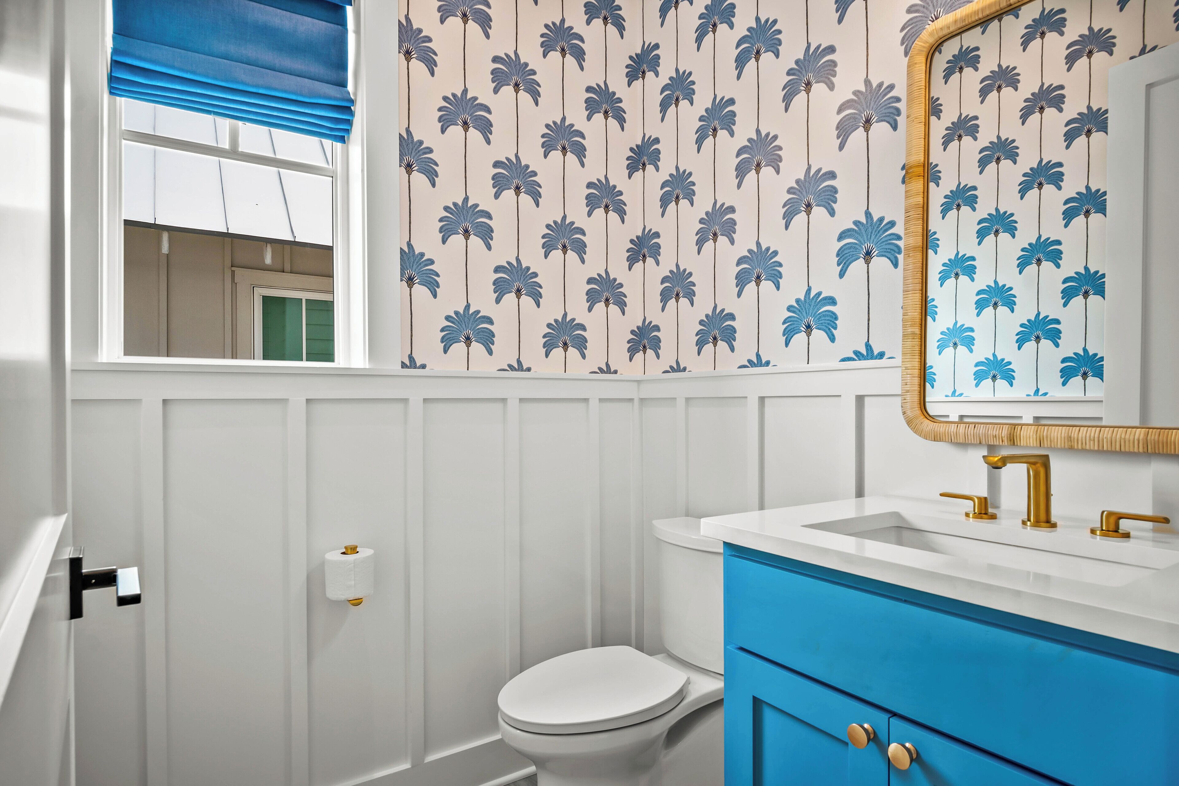 A bathroom with a toilet, a sink with a mirror, and a window with blue blinds.