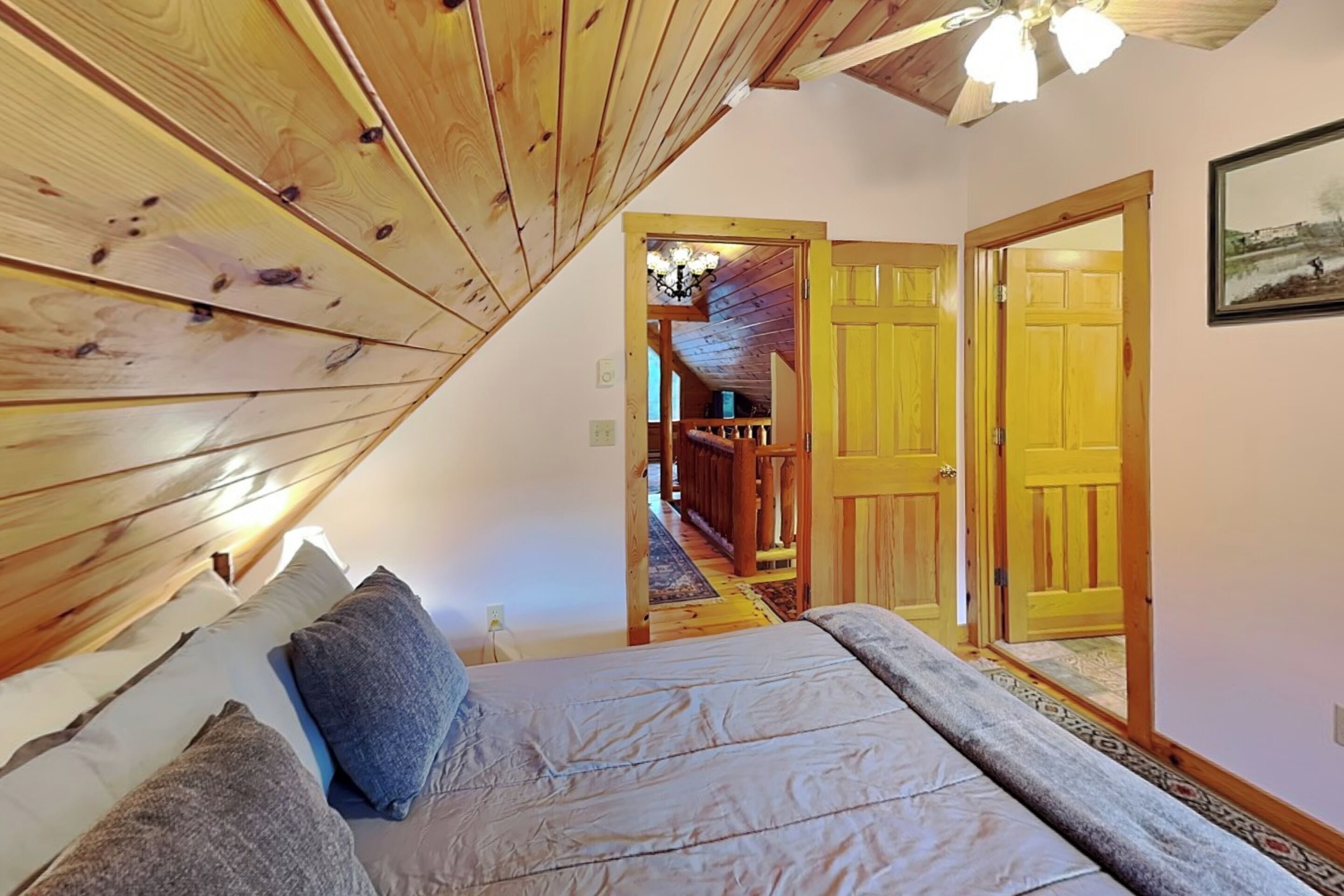 Un dormitorio con techo de madera, una cama con almohadas y un pasillo que conduce a una puerta.