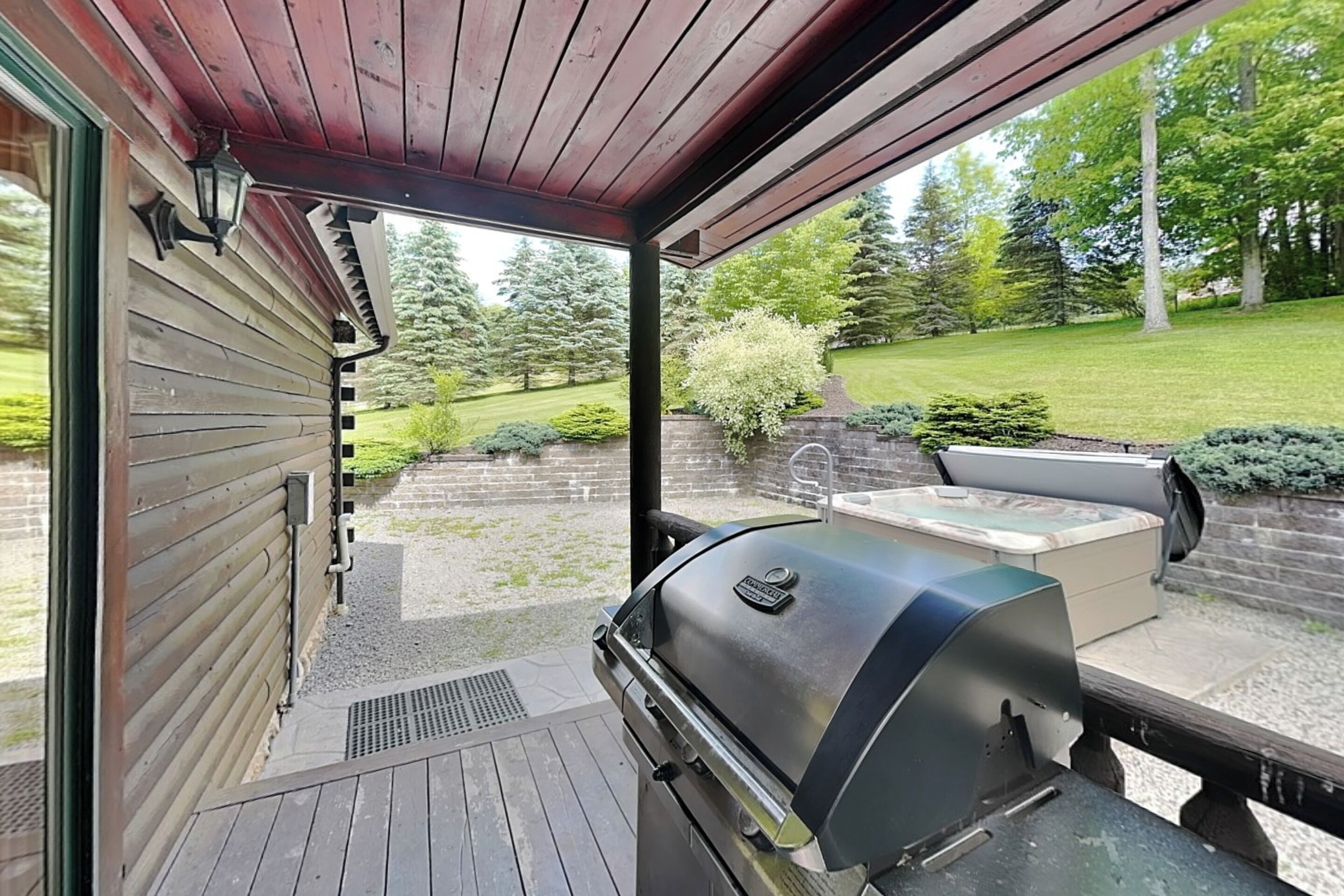 A covered patio with a grill, outdoor seating, and a view of a landscaped garden.