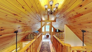 A wooden interior with a central hallway, wooden railings, and a chandelier.
