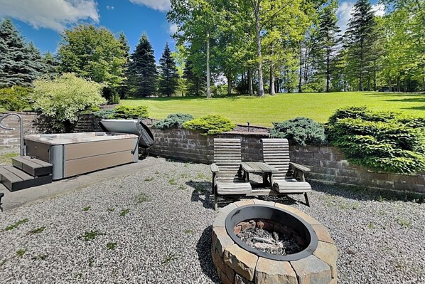 A patio with a stone fire pit, wooden lounge chairs, and a built-in barbecue grill. - The Old World Chalet by Taylor Made Deep Creek (McHenry)