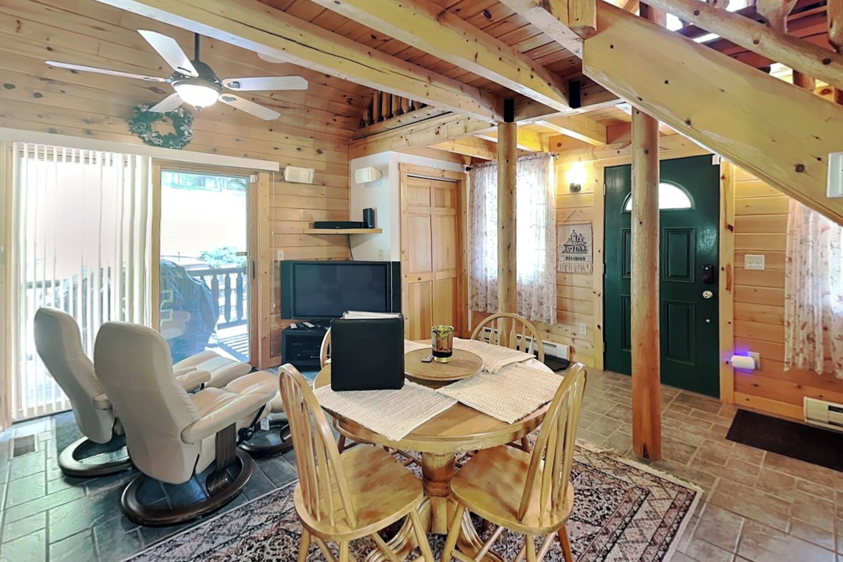 Un intérieur en bois comprenant un coin repas, deux fauteuils massants, un téléviseur et un ventilateur de plafond.