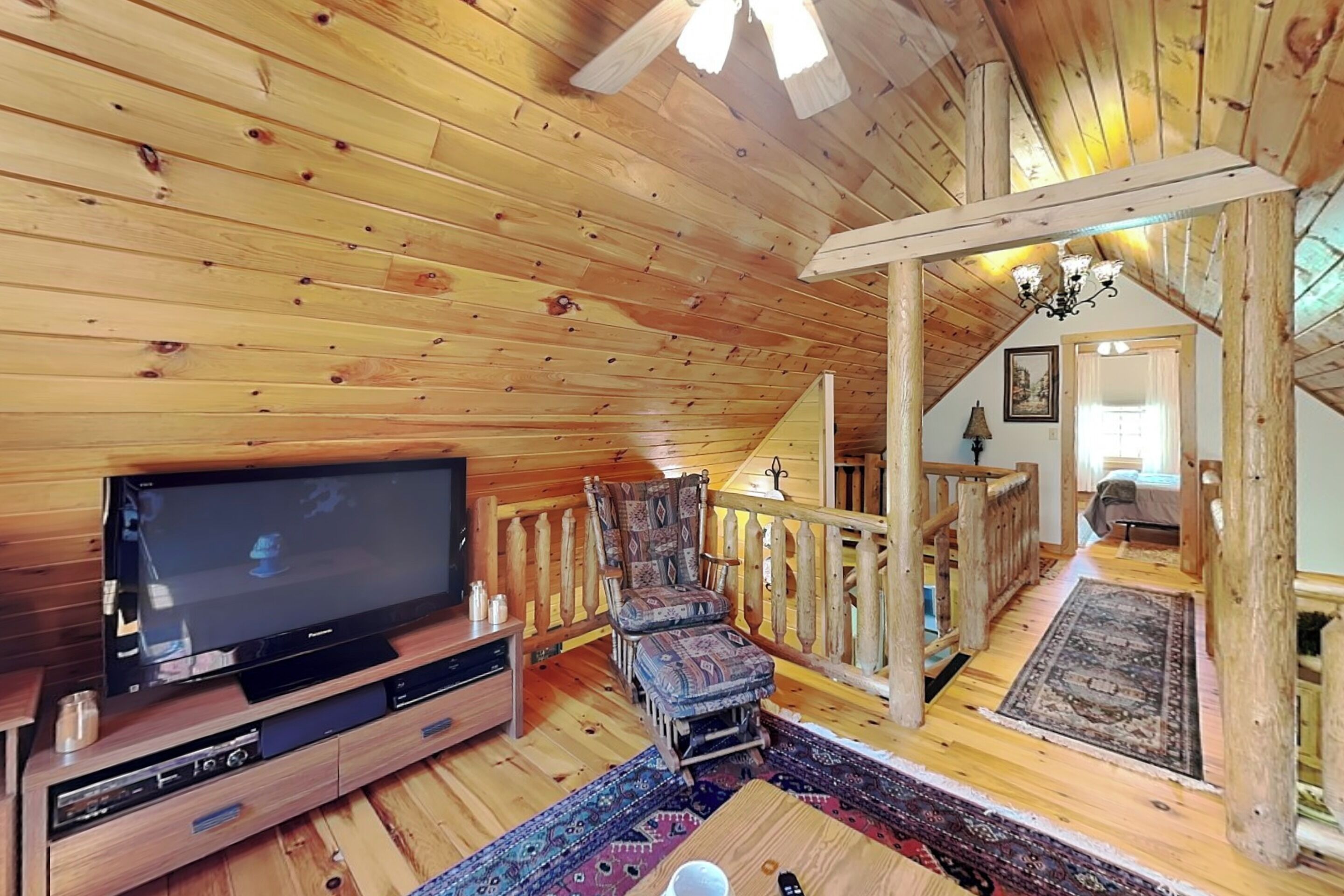 A wooden interior with a television, a patterned chair, a wooden staircase, and a chandelier.
