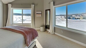 A bedroom with a large window, a bed, a bedside table, and a mirror. - Dacha Verde by Taylor Made Deep Creek (Swanton)