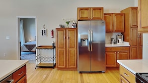 A modern kitchen with wooden cabinets, a stainless steel refrigerator, a coffee maker, and a wine cooler. - Dacha Verde by Taylor Made Deep Creek (Swanton)