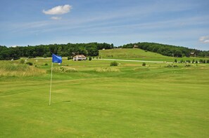 A golf course with a blue flag, green grass, and a house in the background. - Dacha Verde by Taylor Made Deep Creek (Swanton)