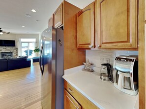 A modern kitchen with wooden cabinets, a stainless steel refrigerator, a coffee maker, and a star-shaped decoration on the countertop. - Dacha Verde by Taylor Made Deep Creek (Swanton)