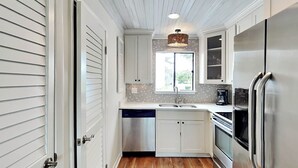 Una cocina compacta con muebles blancos, un refrigerador de acero inoxidable y un lavavajillas.